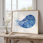 Framed artwork of a blue nautilus on a wooden table with a window in the background